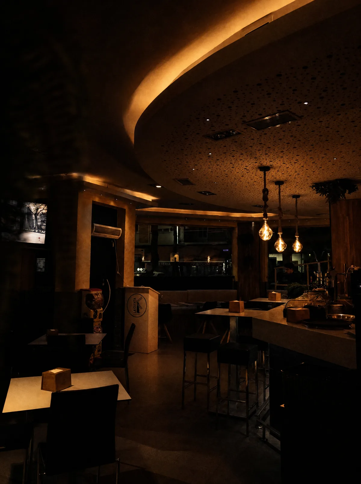 Sala de La Caleta Manchega de noche, con barra alta y lámparas colgantes